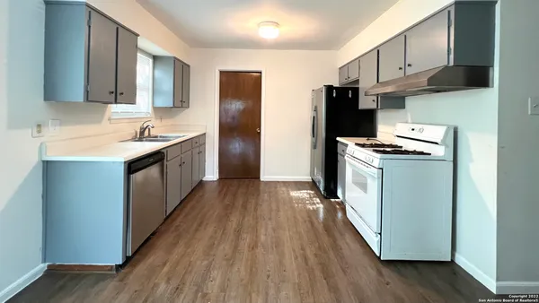 a kitchen with stainless steel appliances granite countertop a refrigerator a sink dishwasher a stove and white countertops with wooden floor