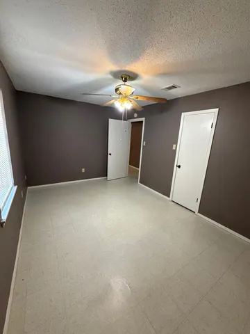 an empty room with a chandelier fan and windows