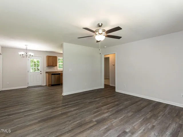 a view of an empty room with wooden floor and a kitchen