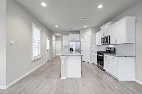 a kitchen with stainless steel appliances granite countertop a stove top oven a sink dishwasher and a refrigerator with wooden floor