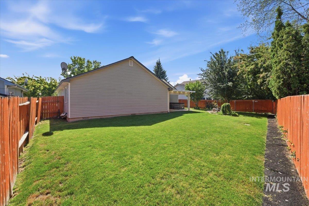 2075 North Springland Place Boise, ID 83713 - Photo 41 of 49 Expansive green lawn surrounded by a privacy fence, featuring a covered patio, mature trees, and established landscaping