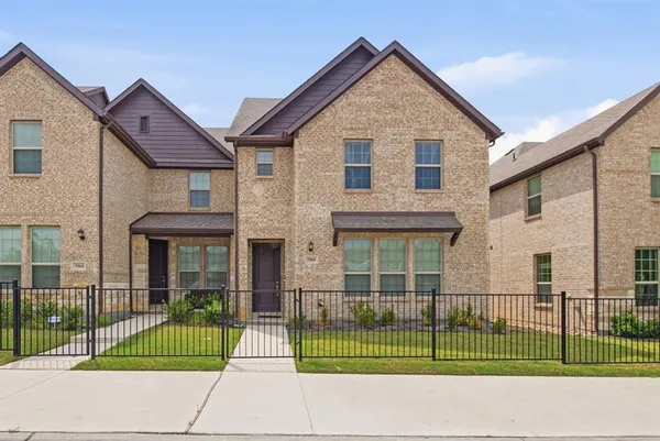 a view of a small house in front of a brick house with large windows