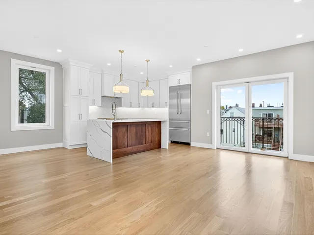 a view of an empty room with kitchen and window