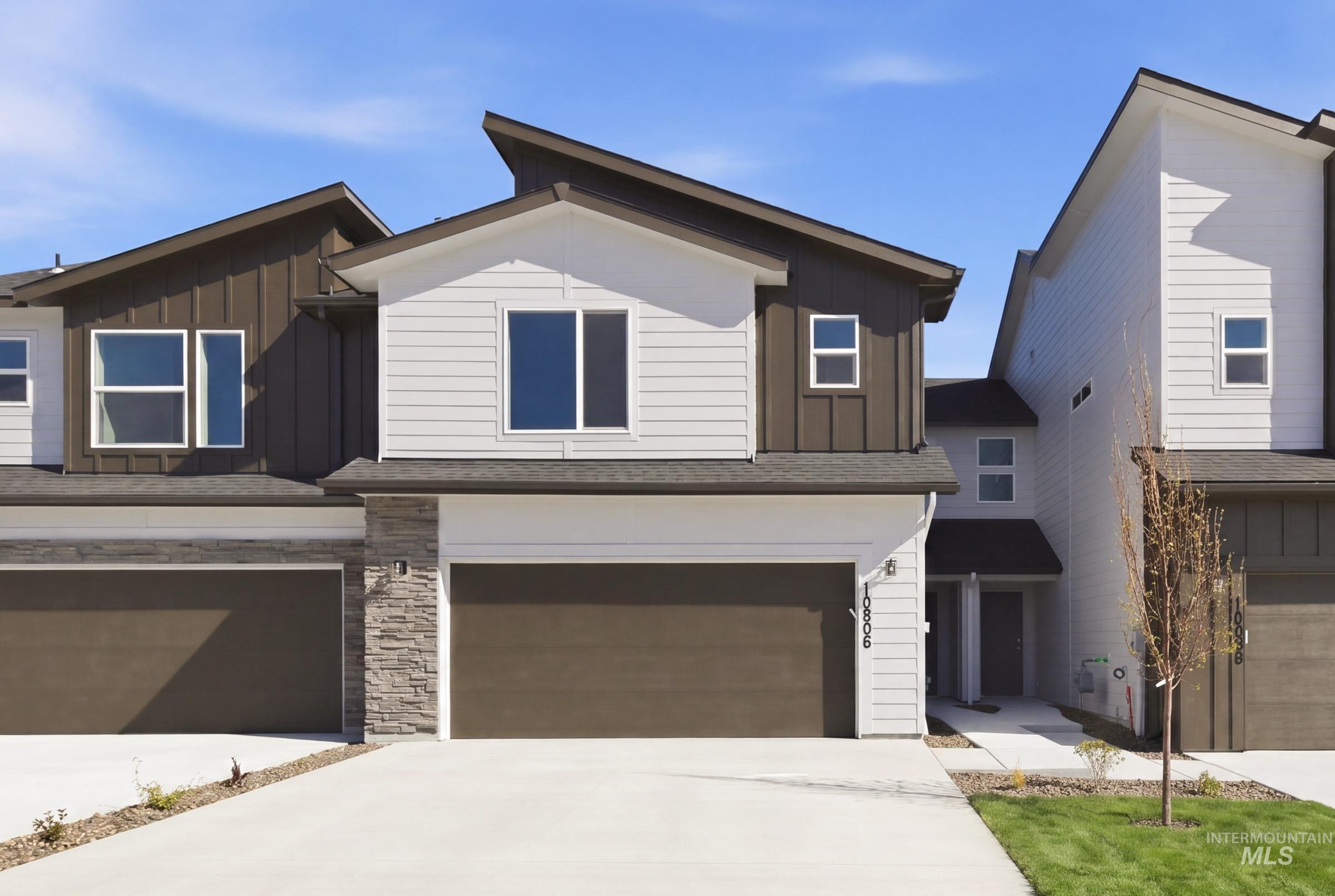 10806 Rutland Street Caldwell, ID 83605 - Photo 1 of 21 Modern townhome exterior featuring an asymmetrical roofline, a two-car garage with a brown door, white siding, dark vertical paneling, and stone accents
