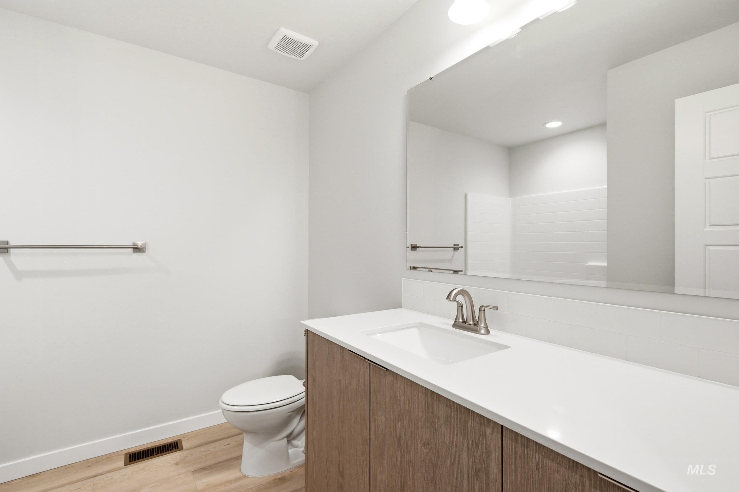 10806 Rutland Street Caldwell, ID 83605 - Photo 16 of 21 Bathroom featuring a wood-finish vanity with a white countertop and integrated sink, a large wall-mounted mirror, a modern toilet, and light wood-finish flooring