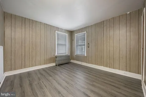 an empty room with wooden floor and windows with curtains
