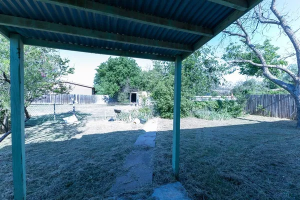 a view of a backyard with large trees and wooden fence