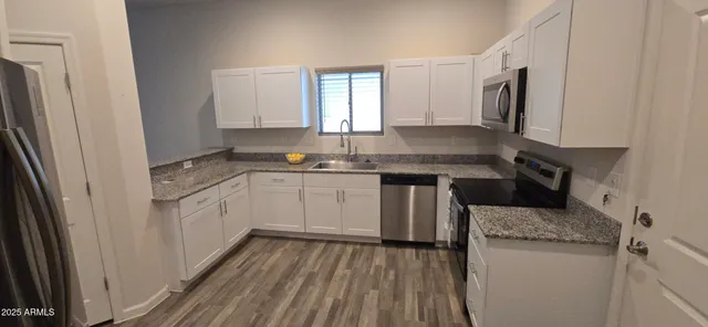 a kitchen with a sink dishwasher a refrigerator and white cabinets with wooden floor