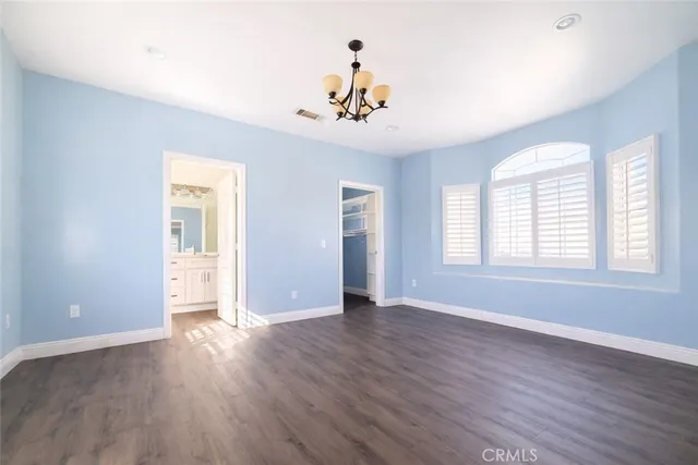 an empty room with wooden floor chandelier and windows