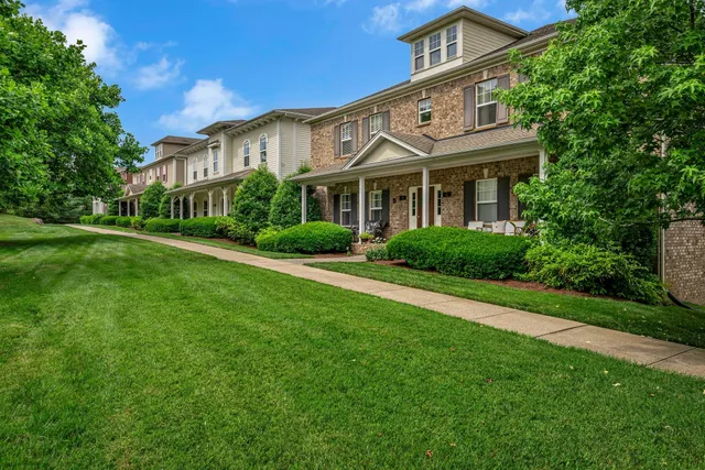 a view of a white house with a big yard and potted plants and large trees