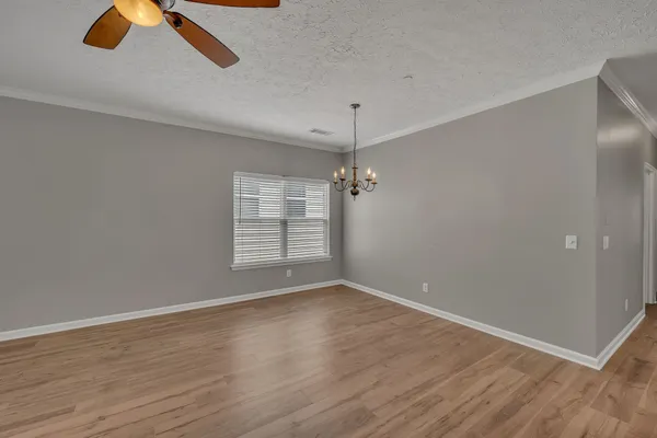 an empty room with wooden floor chandelier fan and windows