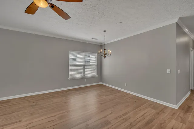 an empty room with wooden floor chandelier fan and windows