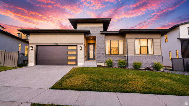 5502 North Valley View Road Lehi, UT 84048 - Photo 1 of 33 Contemporary exterior featuring a stone and stucco facade, a two-car garage with frosted glass panels, and a concrete driveway