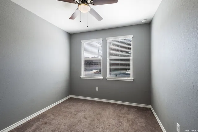 an empty room with chandelier fan and windows