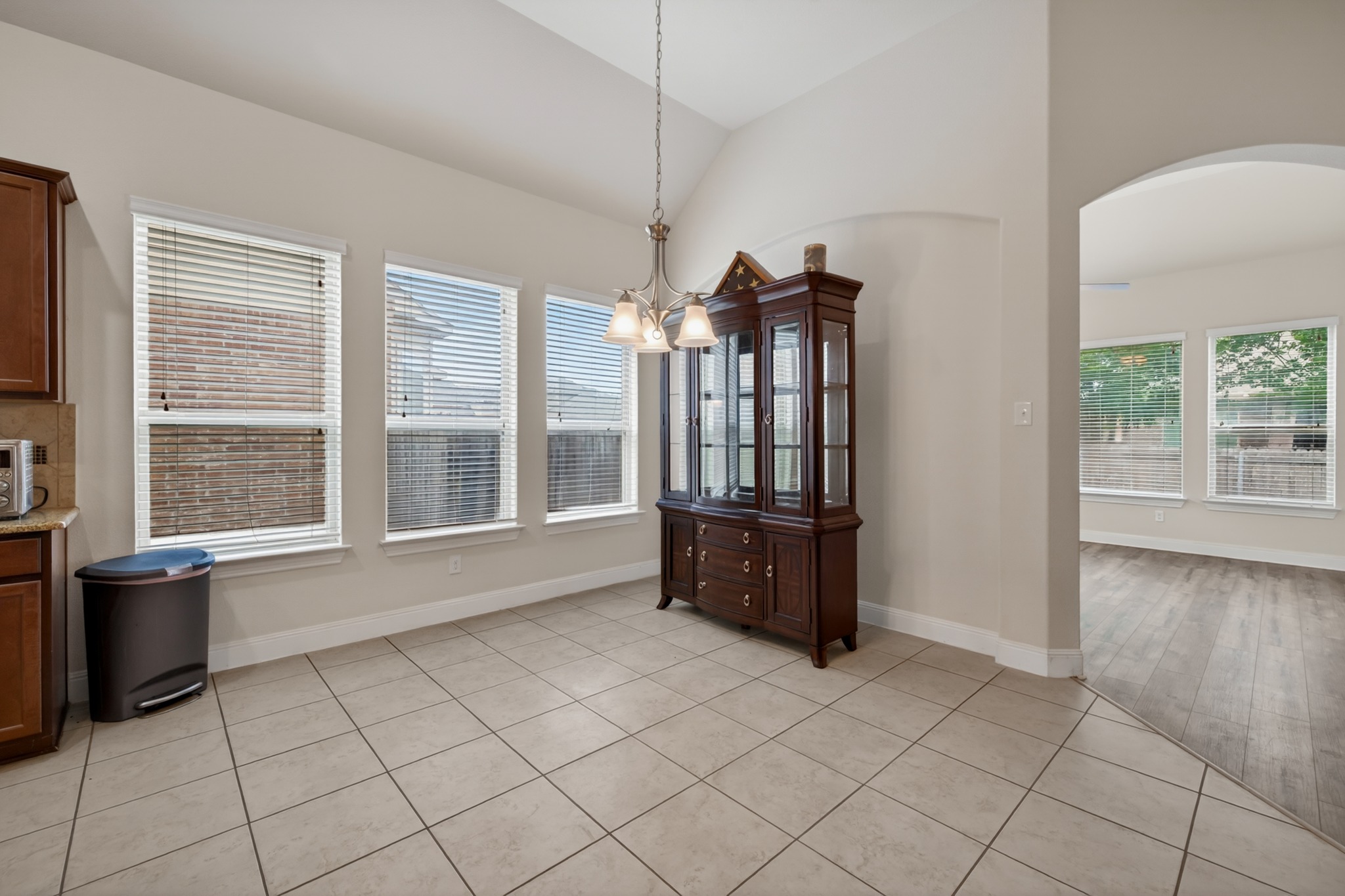 1017 Tabernash Leander, TX 78641 - Photo 9 of 38 Spacious dining area featuring neutral tile flooring, multiple windows with blinds, a vaulted ceiling, and an archway opening to an additional room with wood-finish flooring
