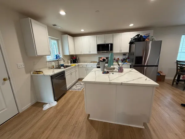 a kitchen with stainless steel appliances a stove a sink a refrigerator a microwave a refrigerator and white cabinets with wooden floor