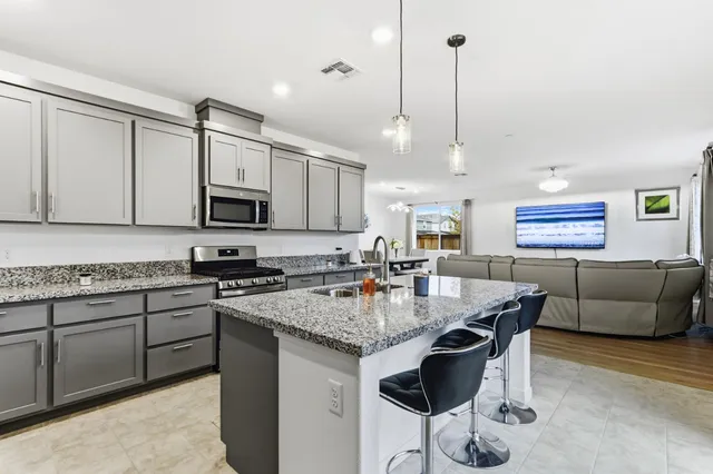 a kitchen with stainless steel appliances granite countertop a stove a sink a microwave a dining table and chairs with wooden floor