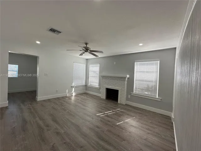 an empty room with wooden floor fireplace and windows