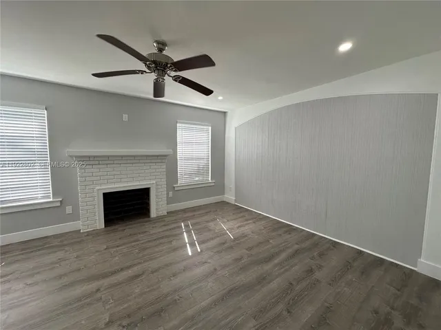 an empty room with wooden floor a ceiling fan a fireplace and windows