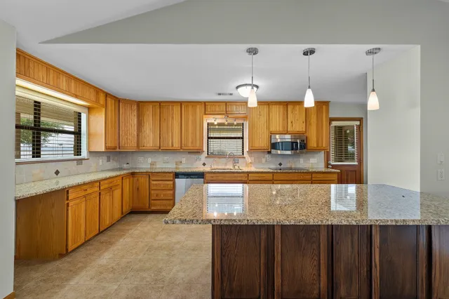 a large kitchen with granite countertop a large counter top cabinets and stainless steel appliances