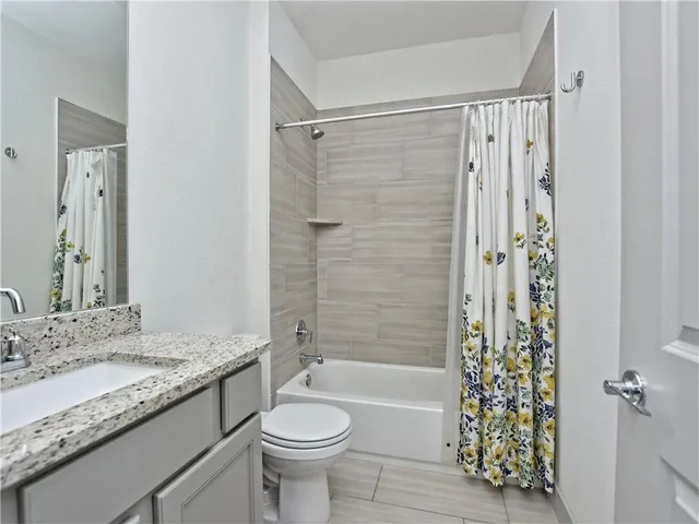 a bathroom with a granite countertop bathtub shower sink vanity mirror and toilet