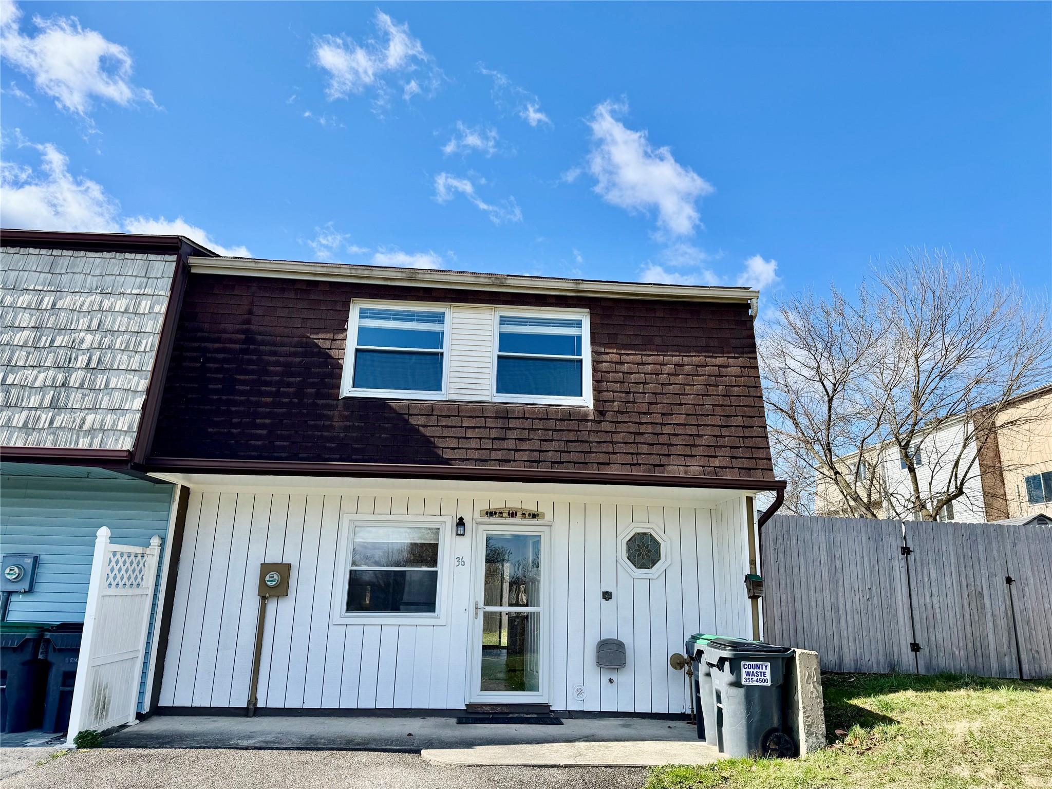 View of front facade featuring mansard roof, fence, and a shingled roof