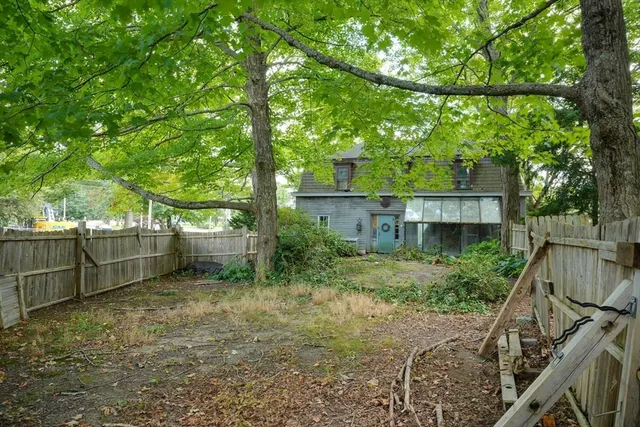 a view of a backyard with large trees and wooden fence