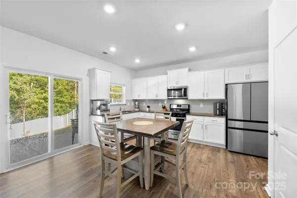 a kitchen with stainless steel appliances a dining table chairs refrigerator and wooden floor