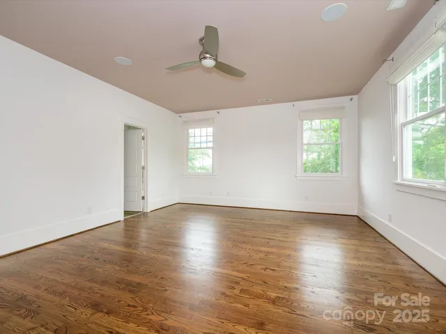 an empty room with wooden floor chandelier fan and windows