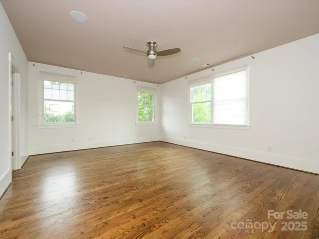 an empty room with wooden floor ceiling fan and windows