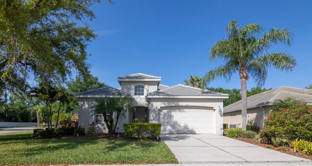 a view of a white house with a flower garden and a large tree