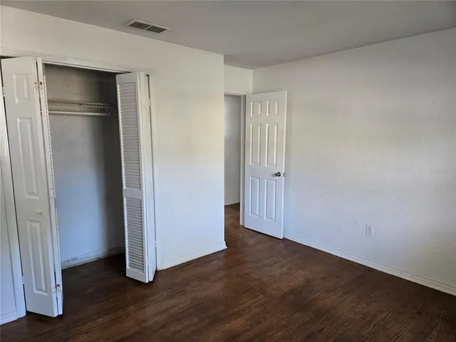 a view of an empty room with wooden floor and closet