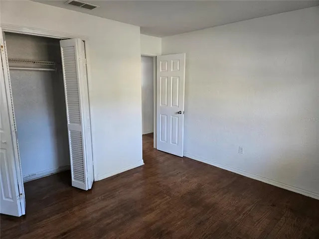 a view of an empty room with wooden floor and closet