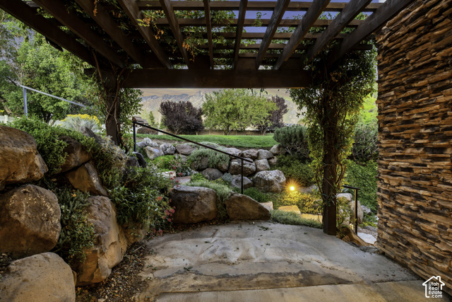 259 Twin River Loop Alpine, UT 84004 - Photo 49 of 61 Private back patio with professionally designed Wood pergola structure with climbing greenery, natural stone retaining walls, metal handrails, integrated landscape lighting, and a stacked stone exterior wall