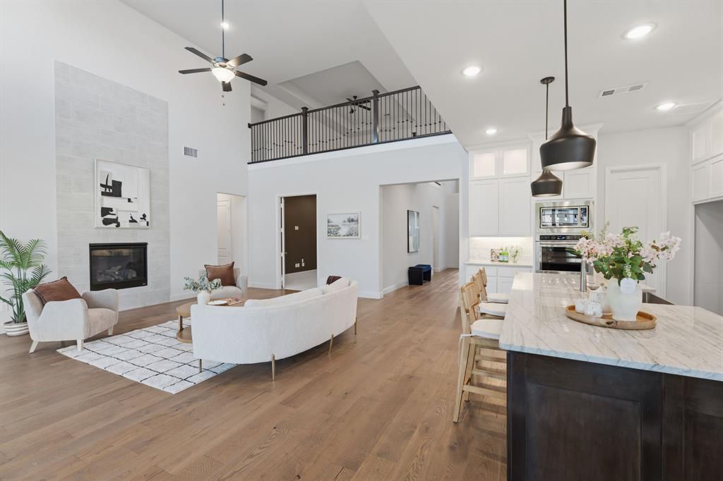 1316 Limestone Ridge Road Mansfield, TX 76063 - Photo 10 of 40 Open-concept interior featuring wood-finish flooring, a two-story tiled fireplace, a second-story balcony with iron railings, a kitchen island with a light-colored countertop, and integrated kitchen appliances