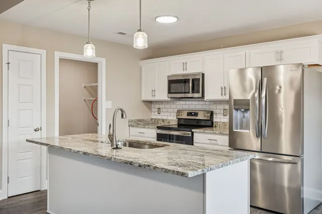 a kitchen with kitchen island granite countertop stainless steel appliances a refrigerator a stove a sink a center island and cabinets