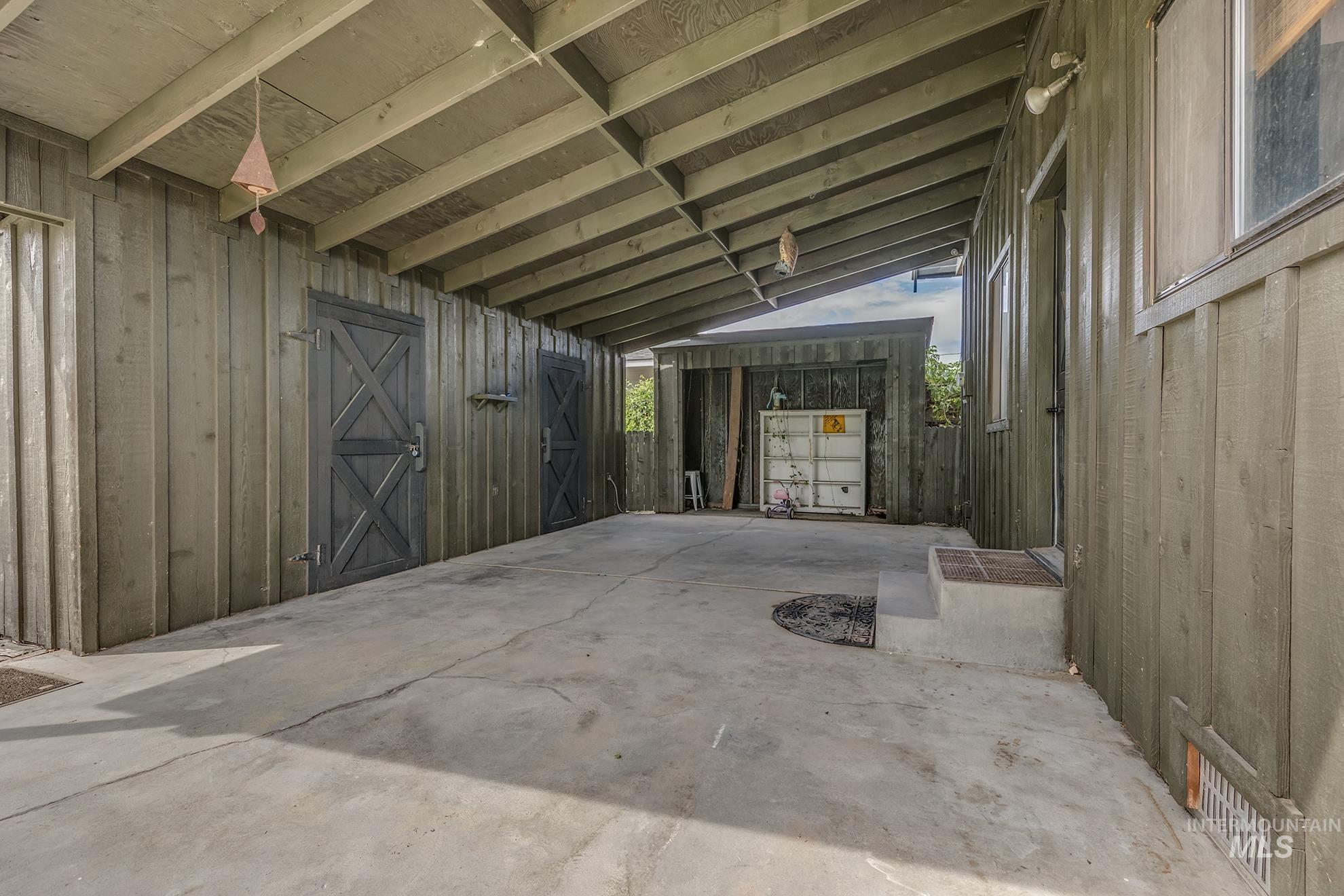 61 Southwest 4th Street Ontario, OR 97914 - Photo 35 of 42 Covered concrete patio featuring exposed beam ceiling, vertical wood siding, two dark-paneled doors with X-brace design, and an exterior light fixture