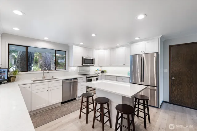 a kitchen with stainless steel appliances a dining table chairs refrigerator and sink