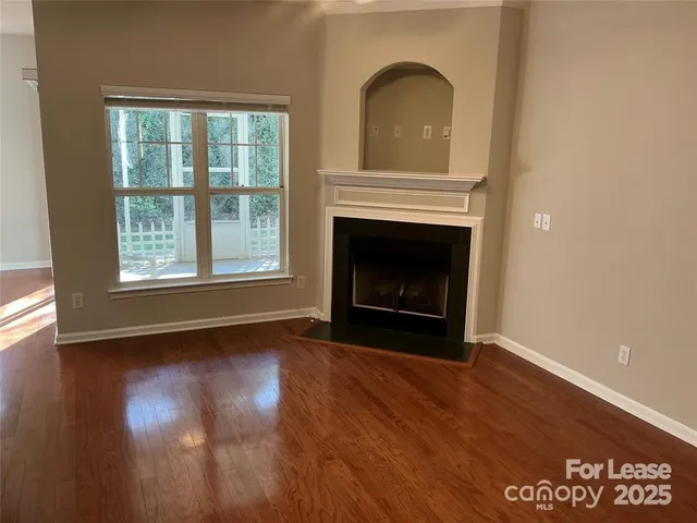 a view of an empty room with wooden floor fireplace and a window