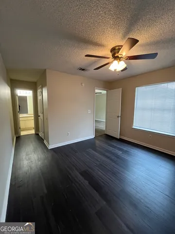 a view of an empty room with wooden floor and a ceiling fan