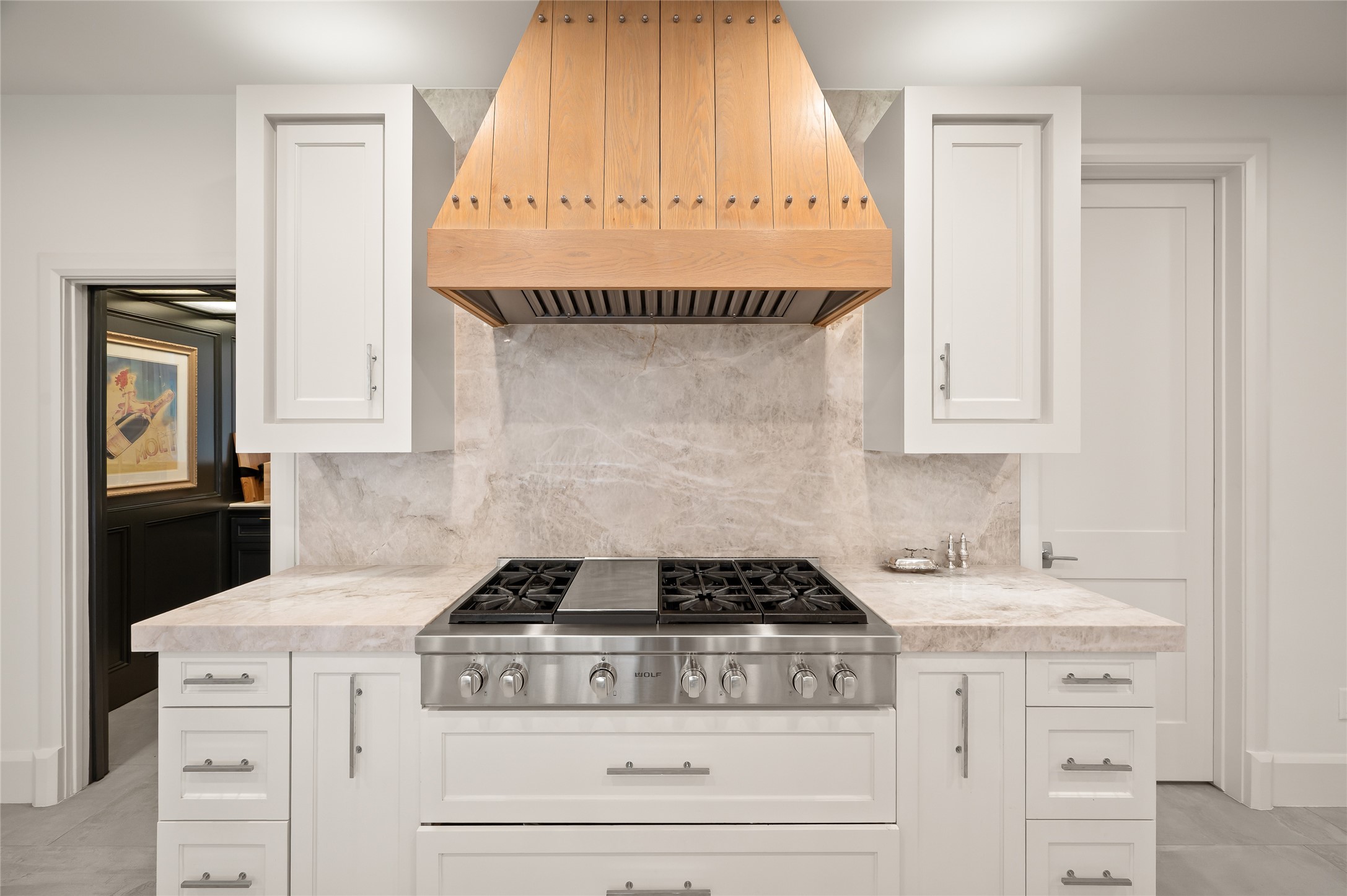 11518 Shadow Way Street Houston, TX 77024 - Photo 13 of 50 A closer look reveals the Wolf gas range set beneath a custom wood vent hood, complemented by polished stone backsplash and crisp white cabinets, balancing refinement with practicality.