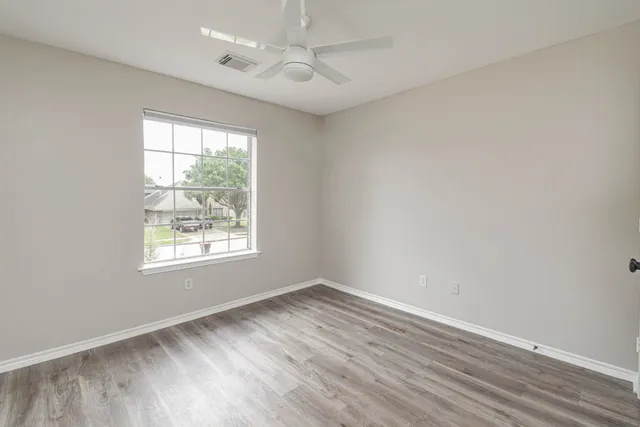 an empty room with wooden floor ceiling fan and windows