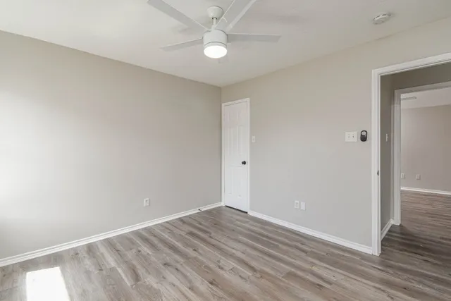 an empty room with wooden floor fan and windows