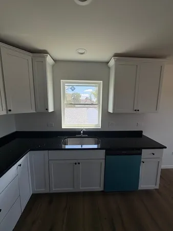 a kitchen with granite countertop white cabinets sink and window