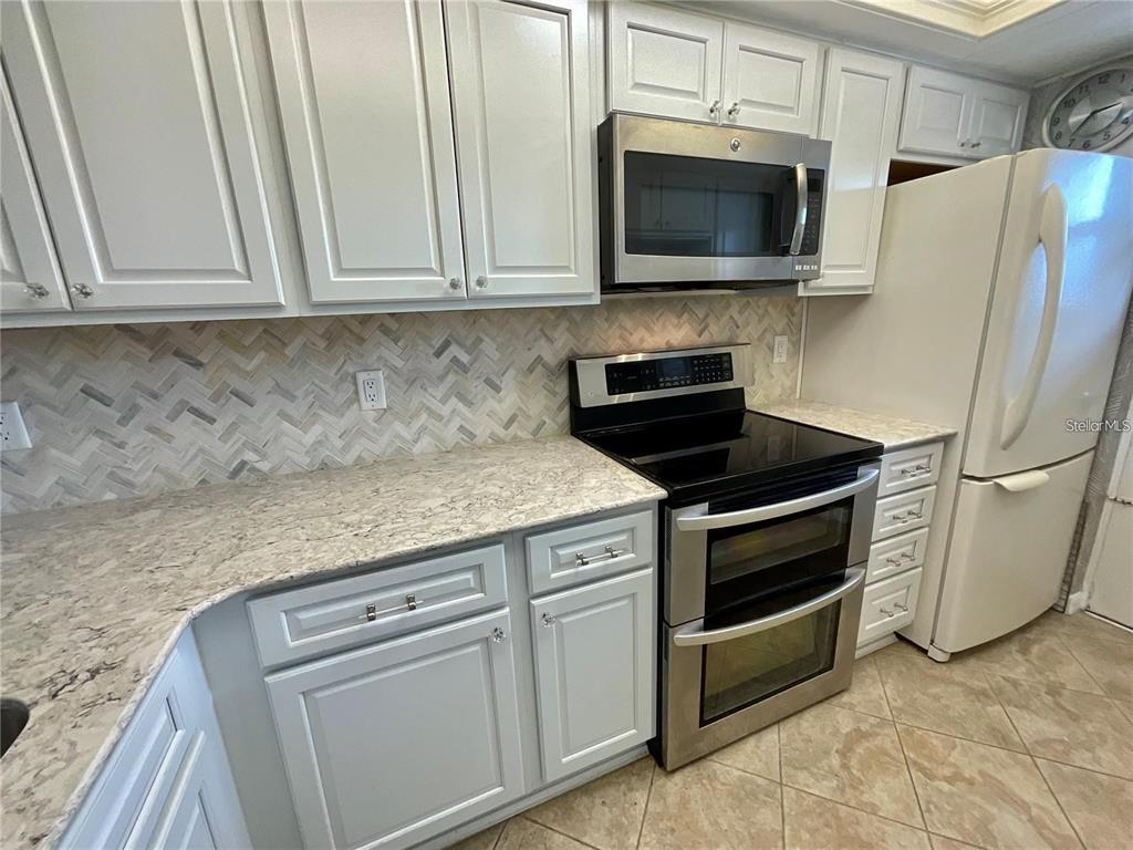 1 Boca Ciega Point Boulevard, Unit 213 St. Petersburg, FL 33708 - Photo 11 of 33 a kitchen with granite countertop white cabinets and stainless steel appliances
