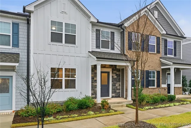 a view of a brick house with a yard plants and large tree