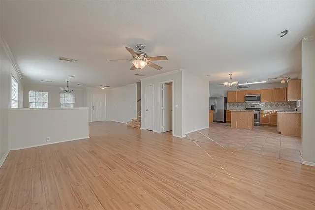 a view of an empty room with wooden floor and a kitchen