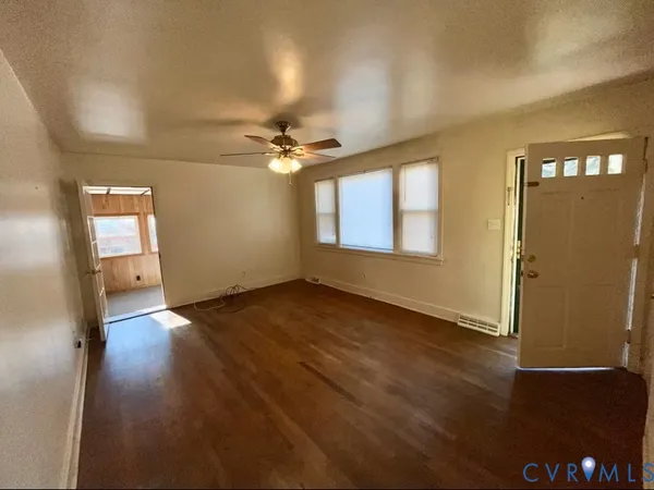 an empty room with wooden floor fan and windows