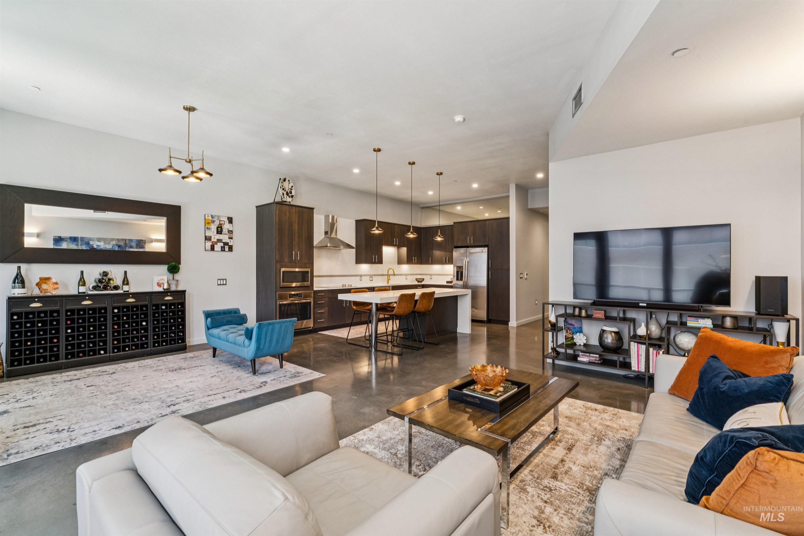 119 South 10th Street, Unit 307 Boise, ID 83702 - Photo 5 of 47 Open-concept living space featuring high ceilings, polished concrete flooring, a gourmet kitchen with stainless steel appliances, a large center island with seating, and a built-in wine storage unit