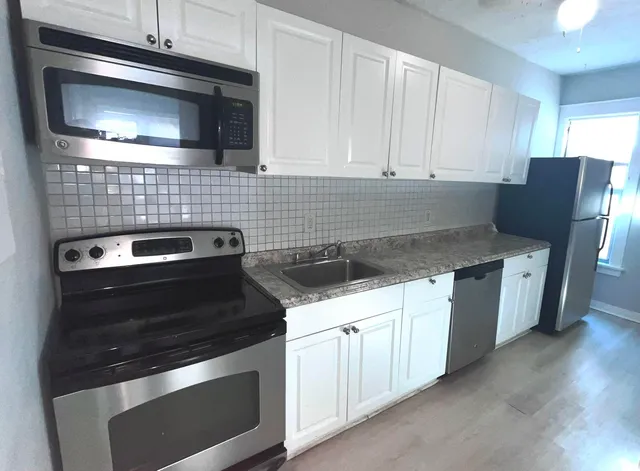 a kitchen with granite countertop white cabinets appliances and wooden floor
